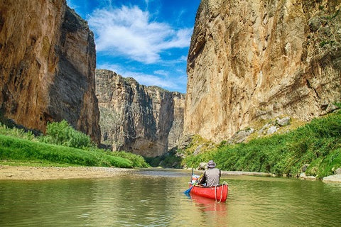 kayaker on a river approaching a canyon wall
